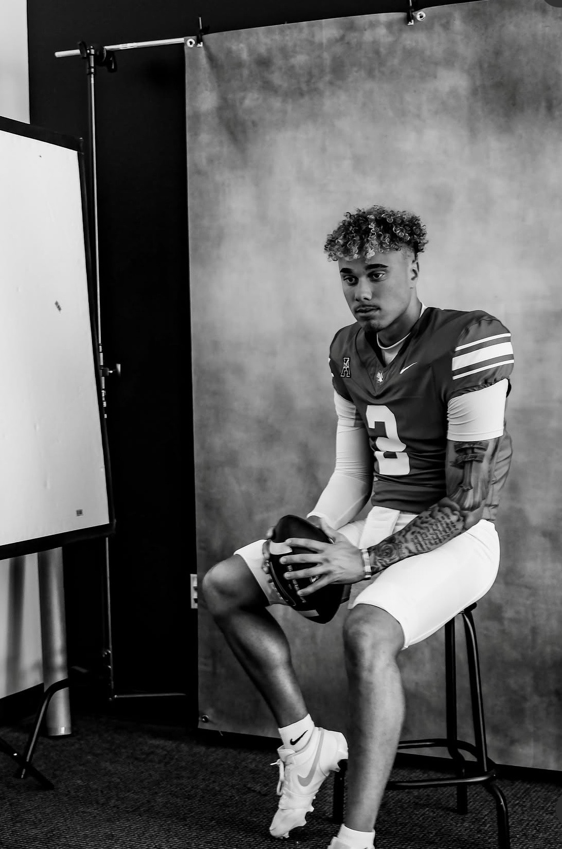 Tayven Jackson seated with a football during a black-and-white portrait session